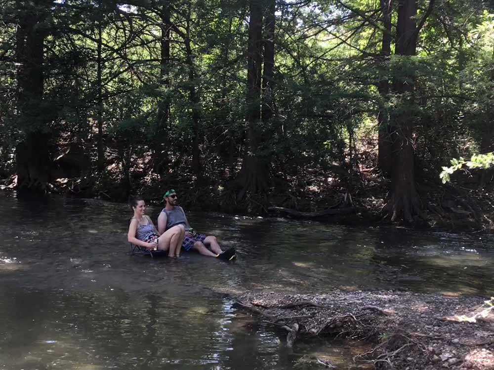 A couple sitting in chairs in the river at BANDERA PIONEER RV RIVER RESORT