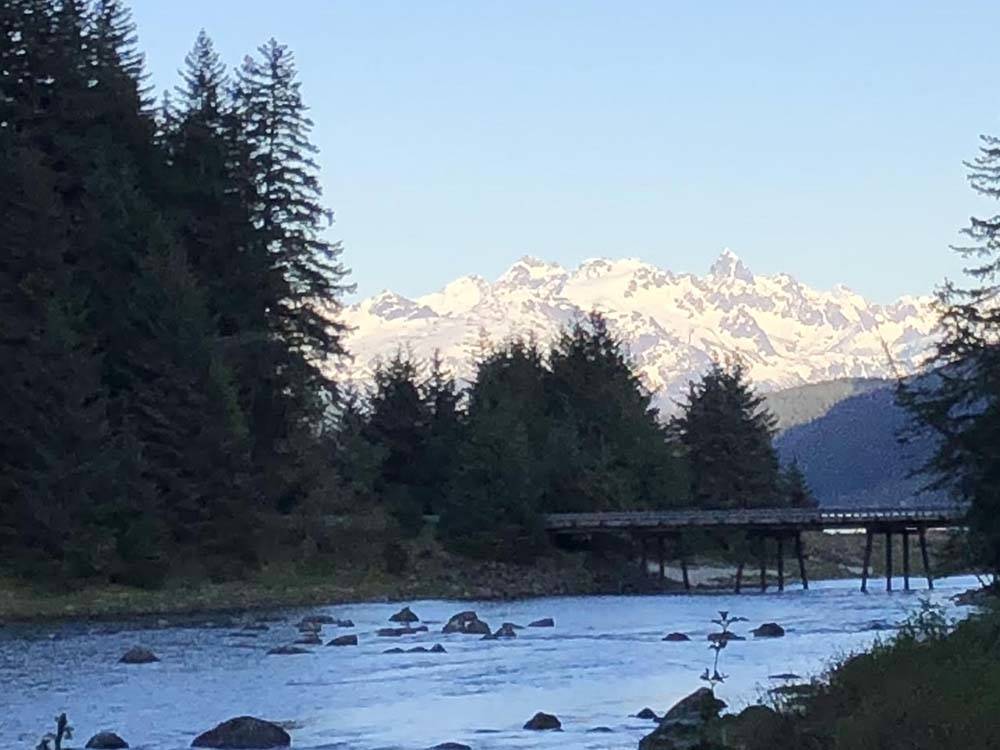 River flows past rocks as snowy mountains loom in background at HAINES HITCH-UP RV PARK