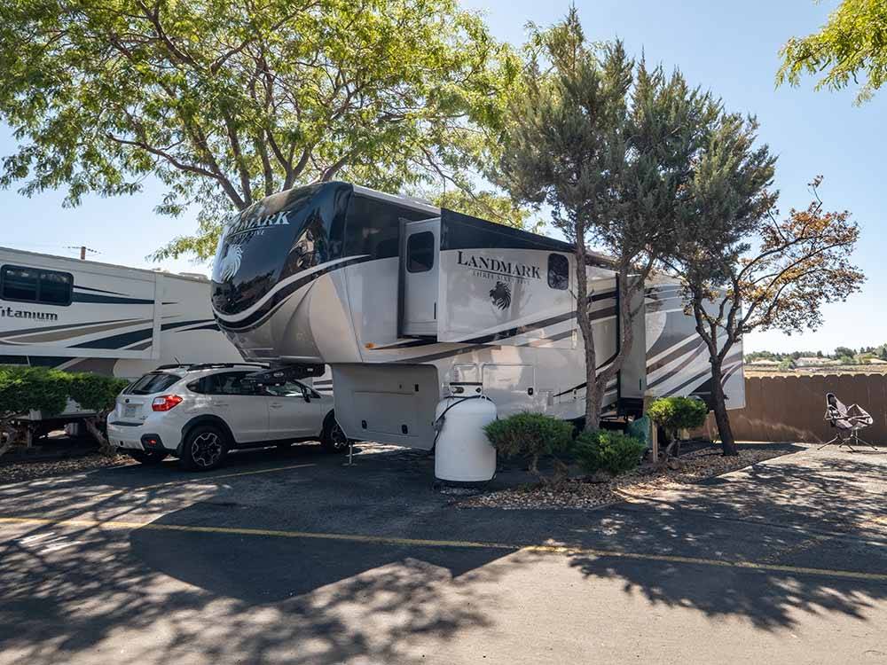 Fifth wheel trailer and car parked in shaded paved site at SHAMROCK RV PARK