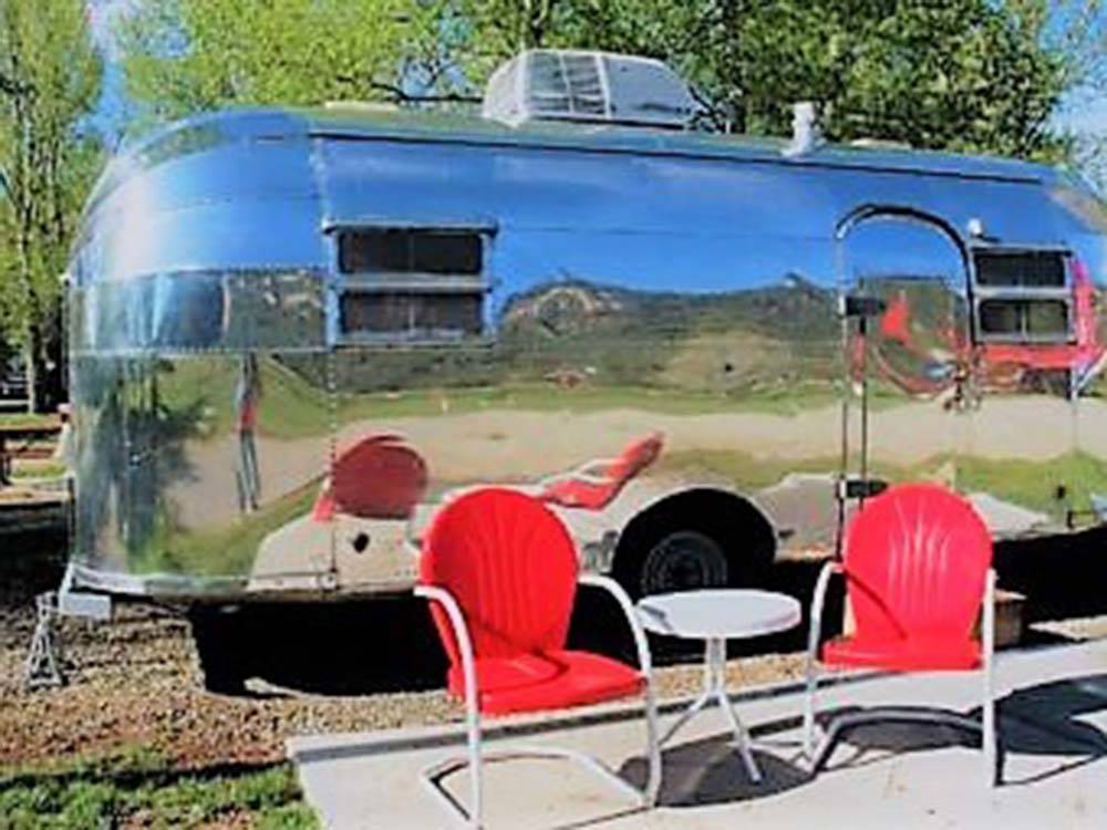Vintage Airstream trailer with red chairs and table at DOLORES RIVER RV RESORT BY RJOURNEY