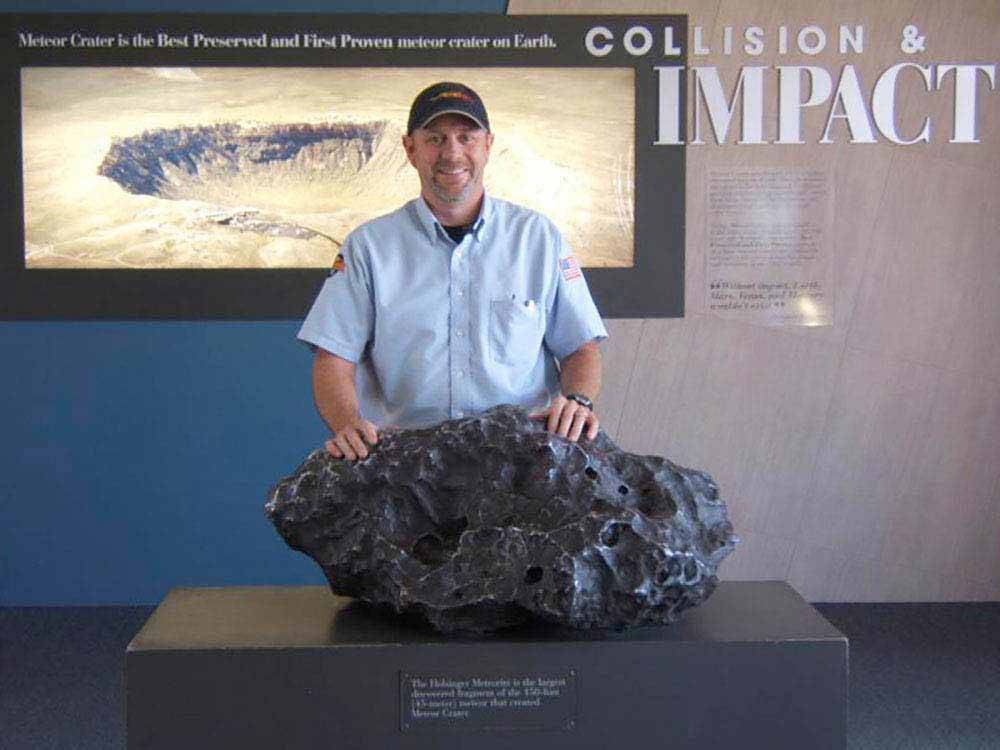 A man standing next to a rock display at the museum nearby at METEOR CRATER RV PARK