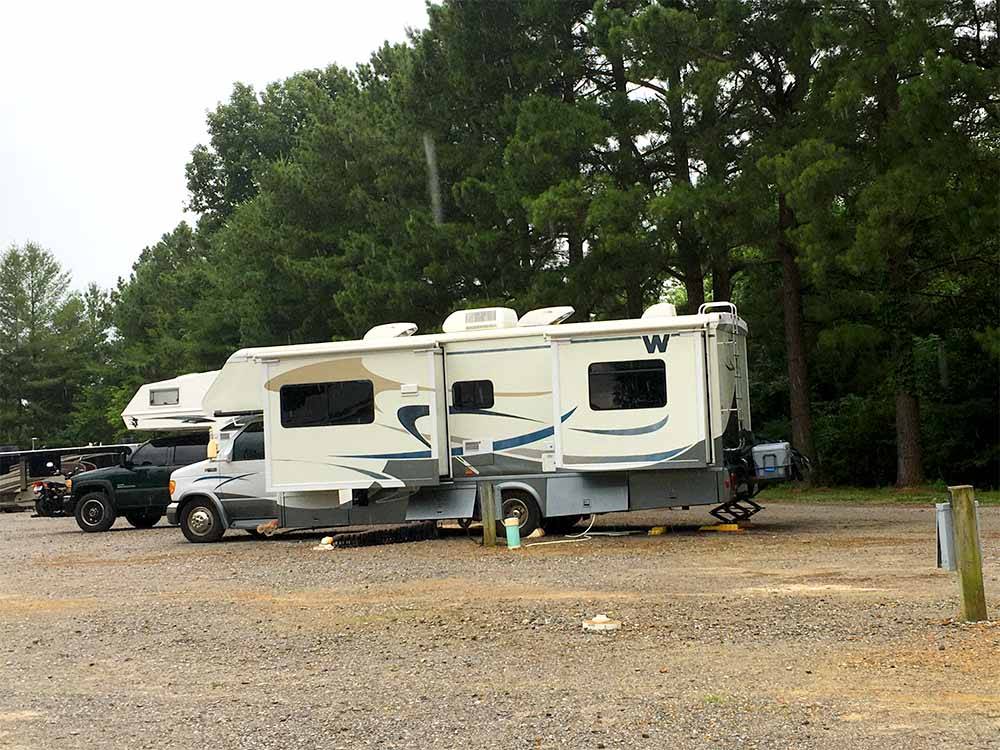 A row of gravel RV sites with trees at FERN LAKE CAMPGROUND & RV PARK