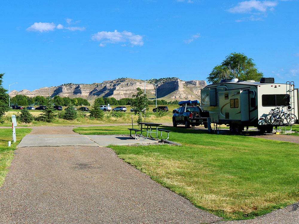 An empty RV site with a picnic table next to site with a fifth wheel hooked up to a truck at ROBIDOUX RV PARK