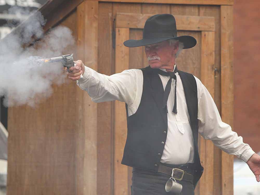 A man in an old west costume shooting a fake gun at CODY YELLOWSTONE