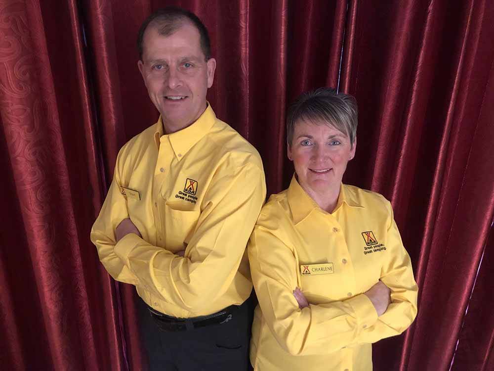 A man and woman with yellow KOA shirts standing in front of a red drape at GROS MORNE/NORRIS POINT KOA