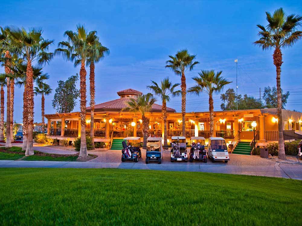 Golf carts parked in front of the lighted up clubhouse at PUEBLO EL MIRAGE RV & GOLF RESORT
