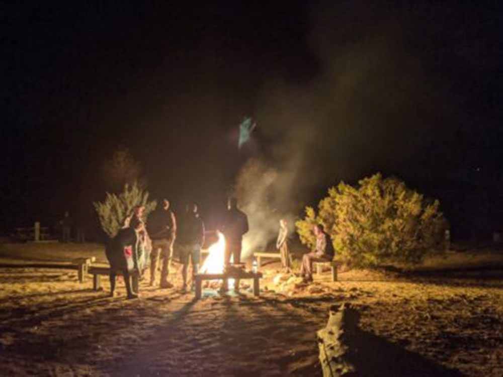 A group of people standing around a fire at night at STAGECOACH TRAILS RV PARK