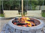 Two bench swings next to a burning fire pit at FIELD & STREAM RV PARK - thumbnail