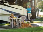A dog sitting in front of a woman with a man holding a cup exiting a Class A RV at LAKESIDE CASINO & RV PARK - thumbnail
