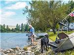 A man fishing with a black dog looking on at CABOOSE LAKE CAMPGROUND - thumbnail