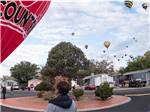 Man looking at red air balloon on the ground with many air balloons in the sky in background at CORONADO VILLAGE RV RESORT - thumbnail
