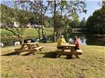 A couple sitting on a picnic bench overlooking the water at VALLEY RIVER RV RESORT - thumbnail