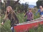 A family carrying a canoe thru grass at BRIGHTON RV RESORT - thumbnail