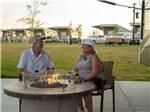 A couple sitting around a gas fire pit at NORTHERN QUEST RV RESORT - thumbnail