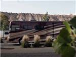 A dark and light brown motorhome in a gravel site at CASTLE GATE RV PARK & CAMPGROUND - thumbnail