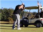 Golfer in back swing next to golf cart at MADISON RV & GOLF RESORT - thumbnail