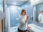 Woman in hoodie brushing teeth in tiled bathroom at CANYON VIEW RV RESORT - thumbnail