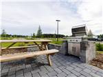 A picnic bench next to a barbecue pit at CHAMPIONS RUN LUXURY RV RESORT - thumbnail