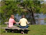 A man and woman on a picnic bench overlooking a river at DENTON FERRY RV PARK & CABIN RENTAL - thumbnail