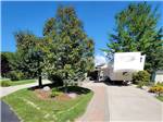 Fifth-wheel on paved site surrounded by trees at TRAVERSE BAY RV RESORT - thumbnail