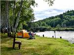 An man in a chair by a tent looking at the river at HOQUIAM RIVER RV PARK - thumbnail