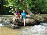 Kids sitting on a rock in the river at CEDAR CREEK RV & OUTDOOR CENTER - thumbnail