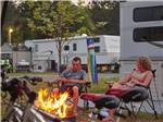 A couple sitting next to a fire pit at their campsite at YOGI BEAR'S JELLYSTONE PARK AT DELAWARE BEACH - thumbnail