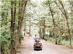 A couple driving a golf cart down a dirt path at NORMANDY FARMS FAMILY CAMPING RESORT - thumbnail