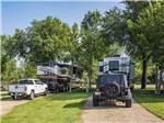 Large RVs in large gravel sites with grass and small trees on either side at CHRIS' CAMP & RV PARK - thumbnail
