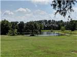 Green field with pond and trees in distance at FORT SMITH-ALMA RV PARK - thumbnail