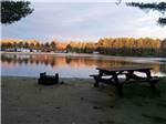 Beach with a picnic table and fire pit at WASSAMKI SPRINGS CAMPGROUND - thumbnail