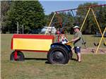 A child playing on a tractor while the dad looks on at HOUGHTON LAKE TRAVEL PARK CAMPGROUND - thumbnail