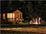 Log cabin with deck with a family standing around a fire pit at PLYMOUTH ROCK CAMPING RESORT - thumbnail