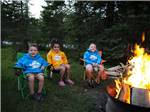 Three young kids sitting by a fire pit at FISHERMAN'S COVE TENT & TRAILER PARK - thumbnail