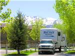 An 5th wheel trailer in a pull thru site with snowcapped mountains in the background at MOUNTAIN SHADOWS RV PARK - thumbnail