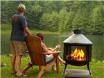Couple sitting next to a large fire pit at LEDGEVIEW RV PARK - thumbnail