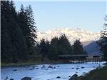 River flows past rocks as snowy mountains loom in background at HAINES HITCH-UP RV PARK - thumbnail