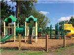 Brightly colored plastic playground with wood chip ground and fence surrounding it at CAHOKIA RV PARQUE - thumbnail