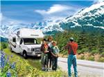 Man taking photos of family in front of RV with mountains in background at ANCHORAGE SHIP CREEK RV PARK - thumbnail