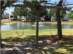 A fountain in the middle of a pond with RVs and swing set on banks at WOODLAND LAKES RV PARK - thumbnail