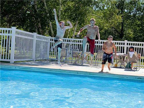 Three young boys jumping into the swimming pool at HOUGHTON LAKE TRAVEL PARK CAMPGROUND