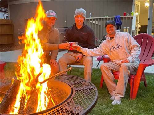 Three men sitting next to a fire pit at RIVERSIDE RV AND CAMPER PARK