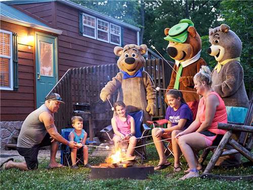 A family roasting marshmallows around a campfire with Yogi Bear at JELLYSTONE PARK AT MAMMOTH CAVE