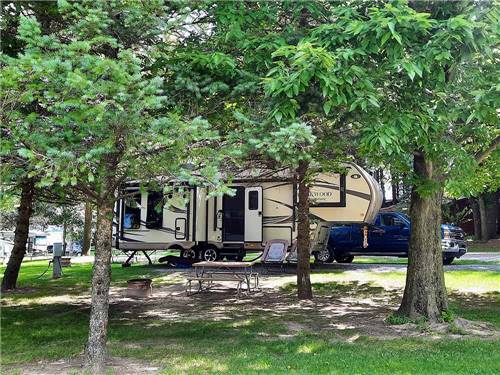 A fifth wheel trailer surrounded by trees at SHIPSHEWANA CAMPGROUND NORTH PARK & AMISH LOG CABIN LODGING