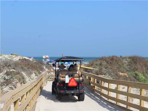A couple in a golf cart driving in a path to the beach at PIONEER BEACH RESORT