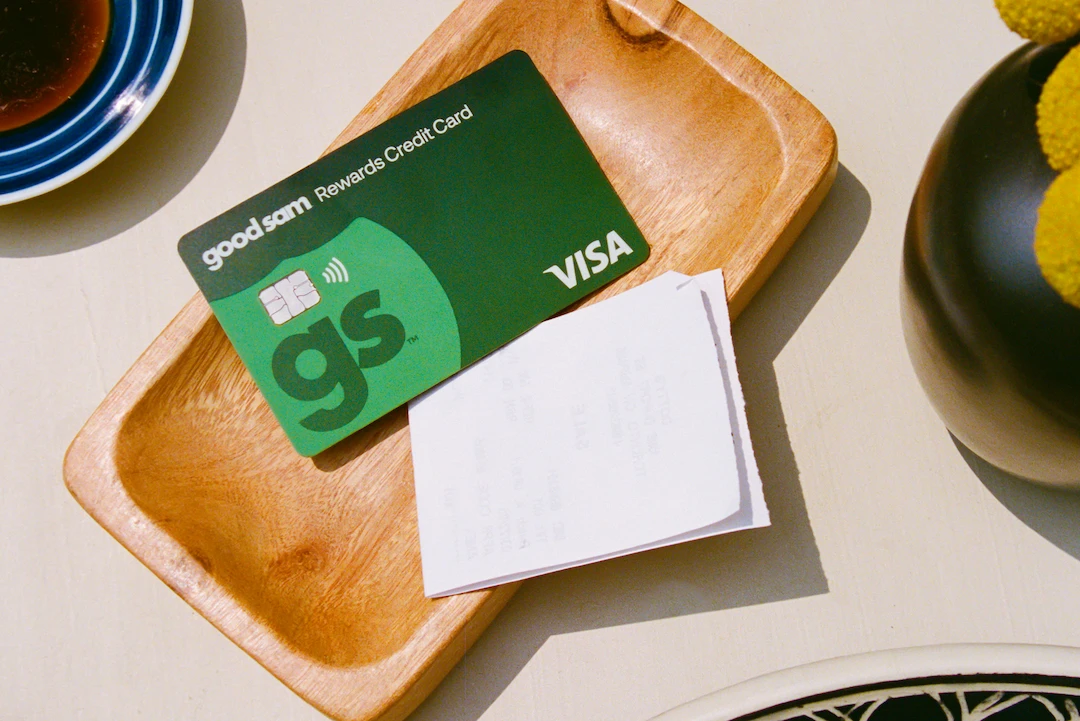 Good Sam Rewards Visa credit card placed on a wooden tray next to a receipt and coffee cup.