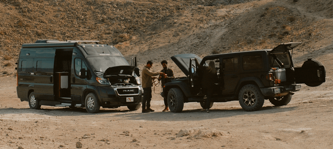 Two men in the desert using an off-road SUV to jumpstart a Class B RV