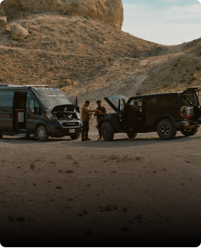 Two men in the desert using an off-road SUV to jumpstart a Class B RV