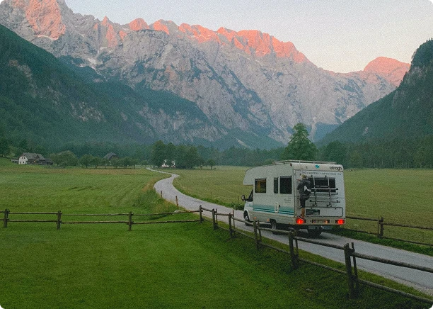 RV driving through a scenic valley with mountains in the background