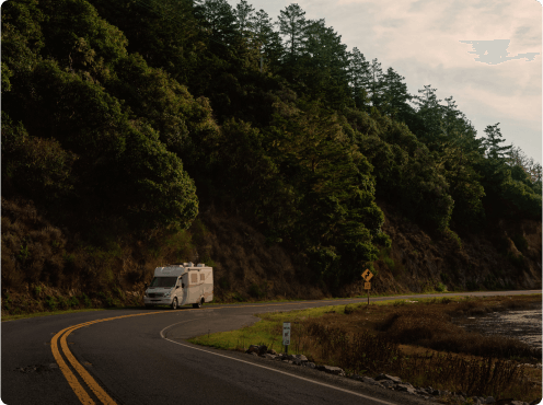 RV driving by water at sunset